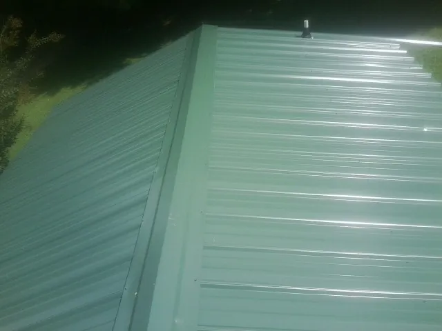 New green metal panels meeting at the ridge of a roof — Flat Roof Repair work by our crew in Cotuit