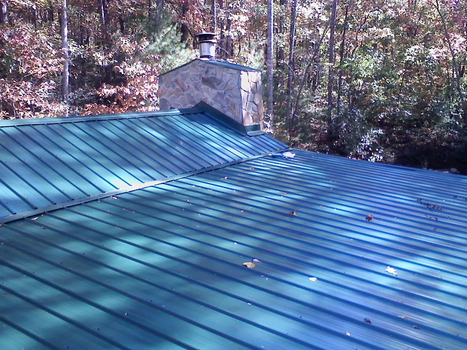 New green metal roof and stone chimney surrounded by autumn woods in Cotuit