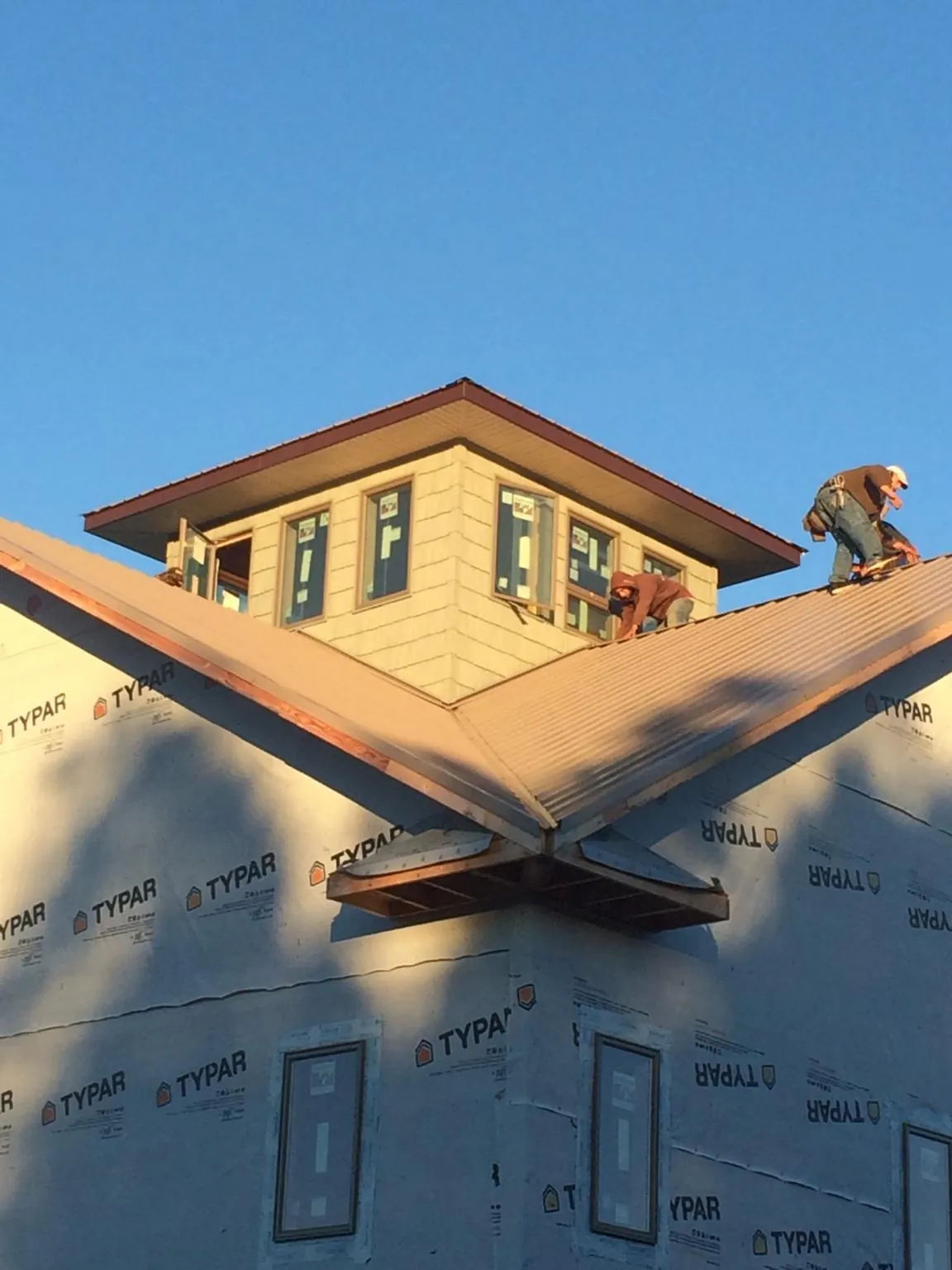 Roofers working around a rooftop cupola on a new metal roof at sunset — Roof Waterproofing in Cotuit by Roofing Brothers